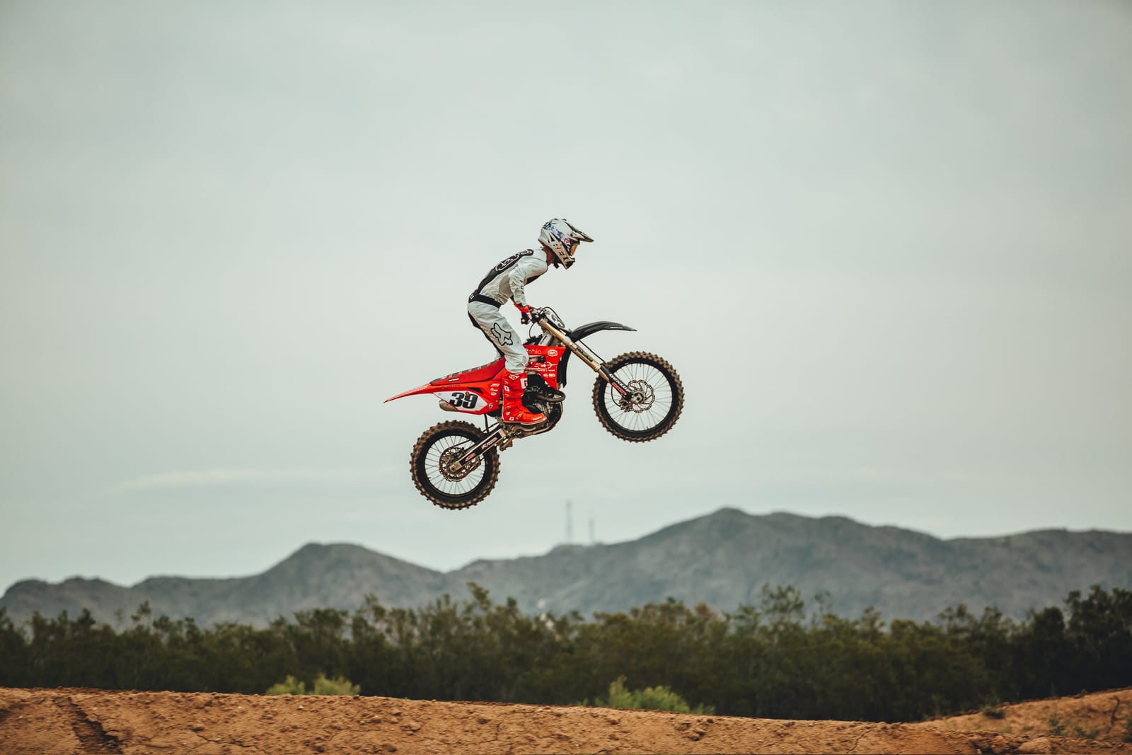 Rider launching a desert motocross jump against an open mountain skyline